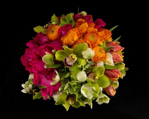 top view of bouquet with hot pink roses, green Cymbidium Orchids, pink Tulips, Hellebores, and orange Ranunculus