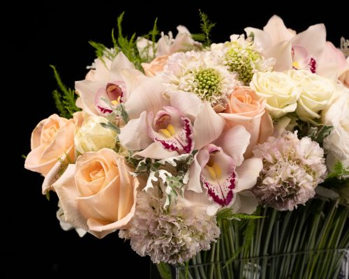 zoomed in bouquet of roses, pale pink cymbidium orchids, scabiosa and calla lilies in a clear vase
