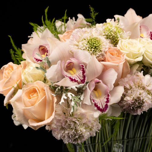 zoomed in bouquet of roses, pale pink cymbidium orchids, scabiosa and calla lilies in a clear vase