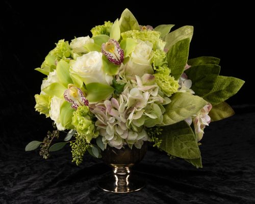 arrangement of cymbidium orchids, roses, lisianthus, and hydrangea with velvet leaves